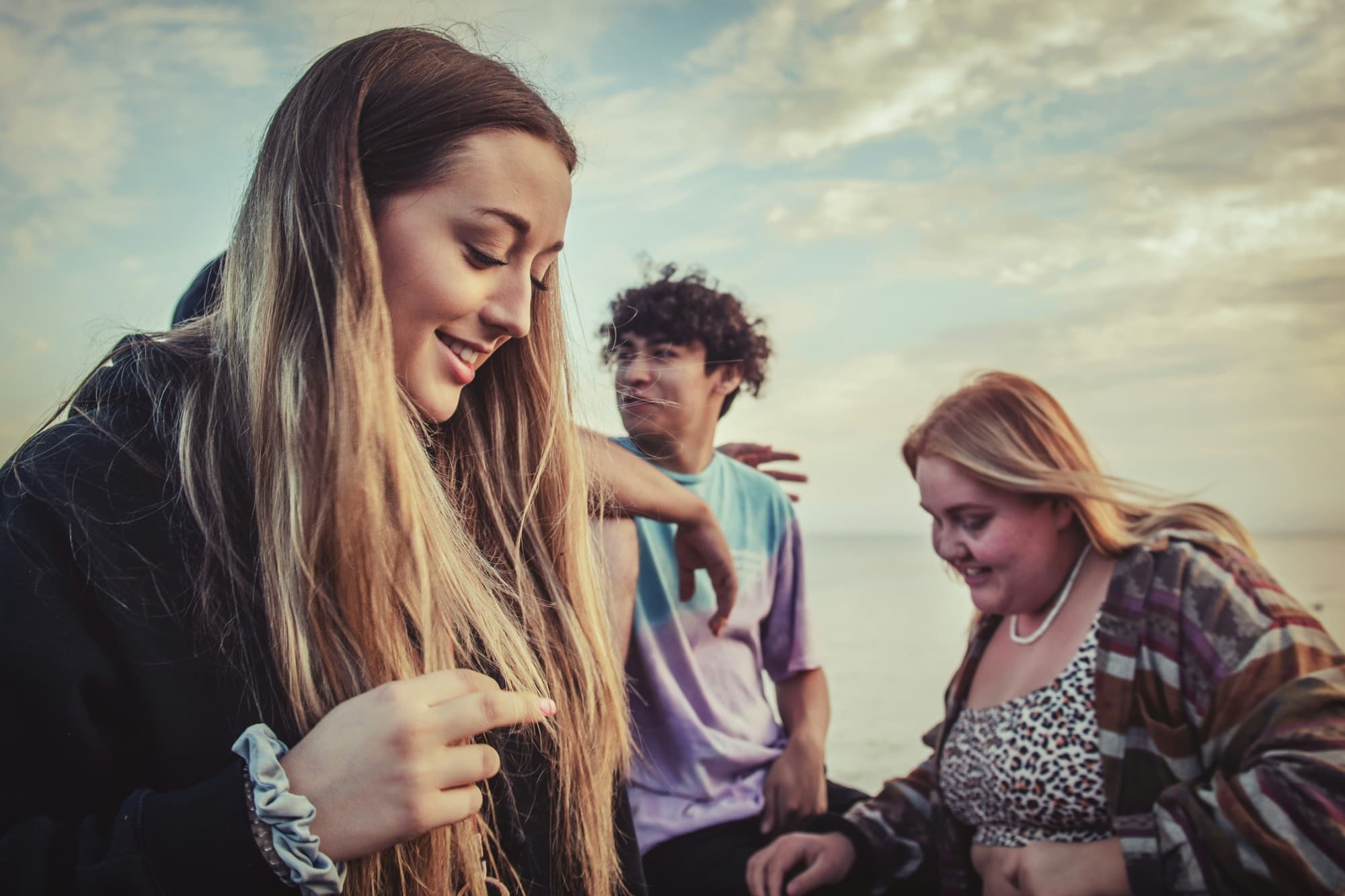 Three friends laughing together by the water at sunset