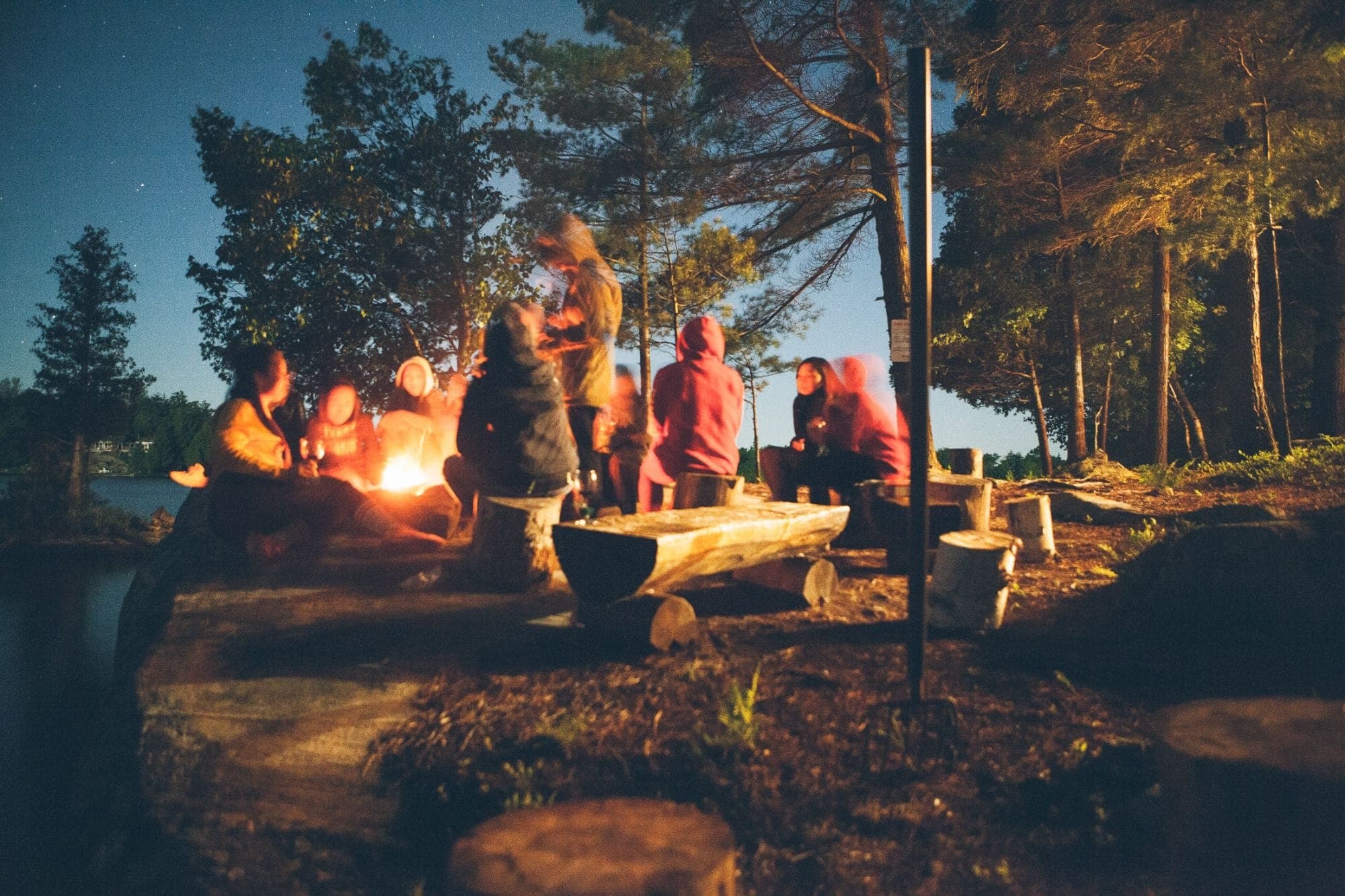 Friends gathered around a campfire by a lake at dusk